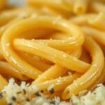 Creamy penne pasta recipe close-up showcasing al dente pasta coated with a rich, cheesy sauce, garnished with freshly grated Parmesan and black pepper.